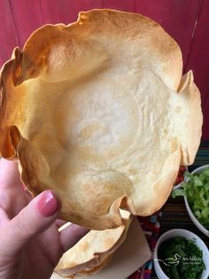 a person holding up a pie crust in front of some salads and other dishes