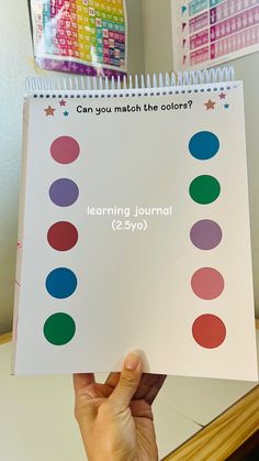 a person holding up a coloring book with colored circles on the cover and writing can you match the colors?