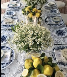 the table is set with blue and white china, lemons, daisies, and baby's breath