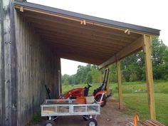 an orange lawn mower sitting in the back of a wooden building next to a metal cart