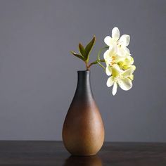 a brown vase with white flowers in it on a table next to a gray wall