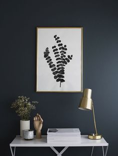 a white desk topped with a lamp next to a painting and a vase filled with flowers