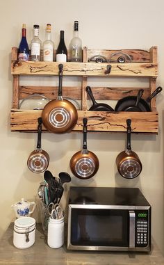 pots and pans are hanging on the wall next to a microwave oven with an open shelf above it