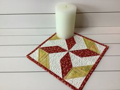 a candle is sitting on top of a quilted coaster with a red and white design