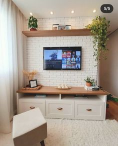 a flat screen tv mounted to a white brick wall in a living room next to a window