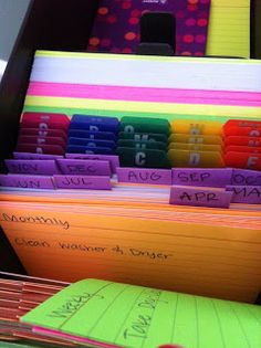 colorful folders are stacked on top of each other in an organized file box with notes attached to them