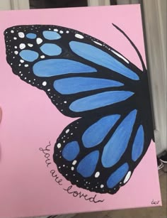 a hand holding up a blue butterfly on a pink background