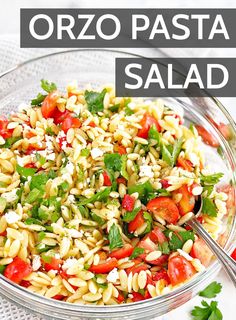 a glass bowl filled with pasta salad on top of a white table next to a spoon