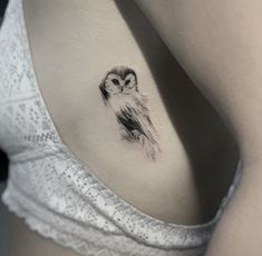 a small owl tattoo on the back of a woman's right shoulder, it is black and white