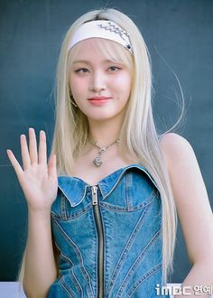 a girl with long blonde hair wearing a denim dress and holding her hand up in the air