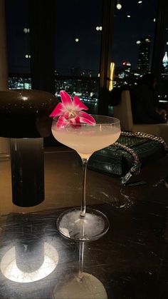 a martini with a pink flower on the rim in front of a cityscape