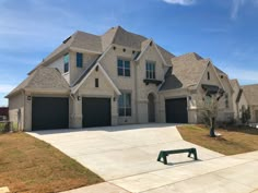 a large house with two garages and a green bench in front of the driveway