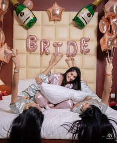 three women laying on a bed with champagne bottles and balloons in the air above them