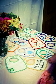 a table topped with lots of baby bibs and vase filled with flowers on top of it