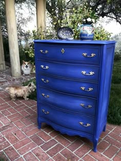 a blue dresser sitting on top of a brick floor next to a white and brown dog