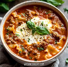 a white bowl filled with pasta and meat soup on top of a gray tablecloth