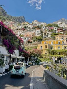 an old car is driving down the road in front of some buildings with flowers growing on them