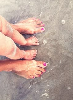 a woman's bare feet with pink nail polish on the beach