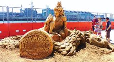 people standing around a sand sculpture on the beach