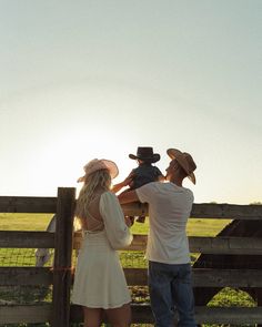 a man and woman standing in front of a fence looking at the sun behind them