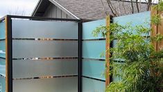 an outdoor privacy wall with metal panels and plants in the foreground, next to a house