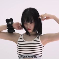 a woman with black hair wearing a white and black striped tank top, holding her hands behind her head