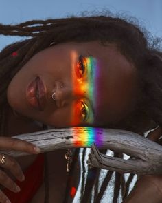 a woman with dreadlocks and rainbow painted on her face is holding a branch