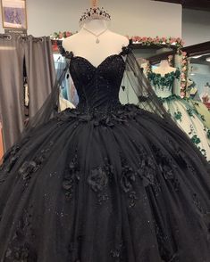 Step into your Quinceanera with elegance and mystery in this stunning black ball gown. This dress is crafted from luxurious tulle and features a dramatic ball gown silhouette with a chapel train that adds a royal finish to your look. The sweetheart neckline and long sleeves exude sophistication, while the intricate beading and appliqued floral details bring a soft yet bold charm to the ensemble. A corset back ensures a perfectly sculpted fit, making this dress as comfortable as it is enchanting. Emo Quinceanera, Black Quince Theme, Quinceanera Dresses With Flowers, Black Ball Gown Dress, Long Sweet 16 Dresses, Dresses With Flowers