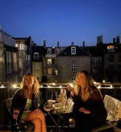 two women sitting at a table with wine glasses in front of them on a balcony