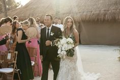 a bride and groom are walking down the aisle at their wedding ceremony in front of an thatched hut