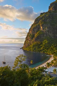 a boat is on the water next to a mountain and some palm trees in front of it