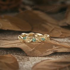 two gold rings with green stones sitting on top of leafy brown leaves in the background