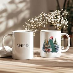 two coffee mugs sitting on top of a wooden table next to a vase with flowers