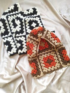 two crocheted beanies are laying on a white sheet with black and orange squares