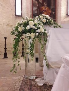 white flowers are in a tall vase on the floor next to a chair and table cloth