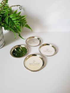 four silver plates sitting on top of a white table next to a potted plant