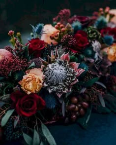 a bunch of flowers that are on top of a blue table cloth with leaves and berries