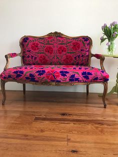 a pink couch sitting on top of a hard wood floor next to a vase with flowers