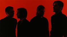 three men standing in front of a red background with one man looking at the camera