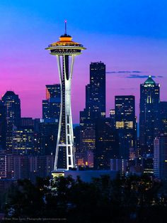 the space needle in seattle at night with city lights and skyscrapers lit up behind it