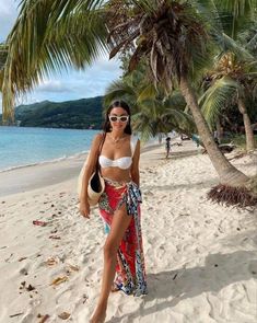 a woman standing on top of a sandy beach next to the ocean and palm trees