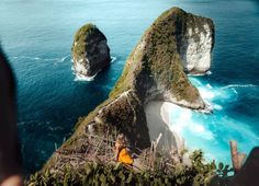 two large rocks sticking out of the ocean next to each other with people standing on them