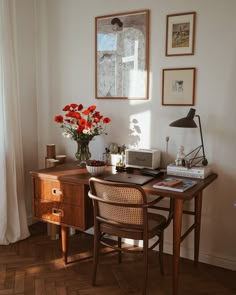 a wooden desk topped with a laptop computer next to a vase filled with red flowers