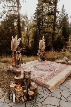 an area rug with candles and flowers on it in the middle of a forest filled with tall trees