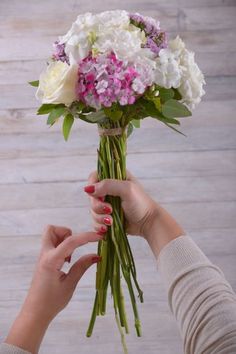 two hands holding a bouquet of white and purple flowers