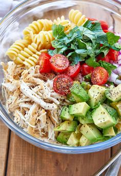 a glass bowl filled with pasta salad on top of a wooden table