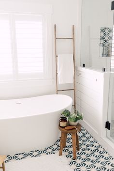 a white bath tub sitting under a window next to a wooden ladder in a bathroom