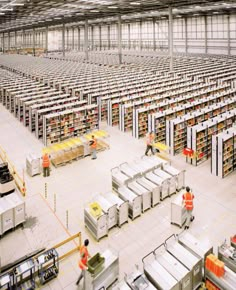 an industrial warehouse filled with lots of shelves and workers in orange vests working on the racks