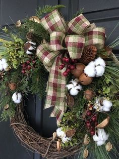 a wreath with cotton, pine cones and berries hanging on the front door for christmas