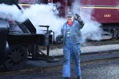 a man standing next to a train with steam coming out of it's engine